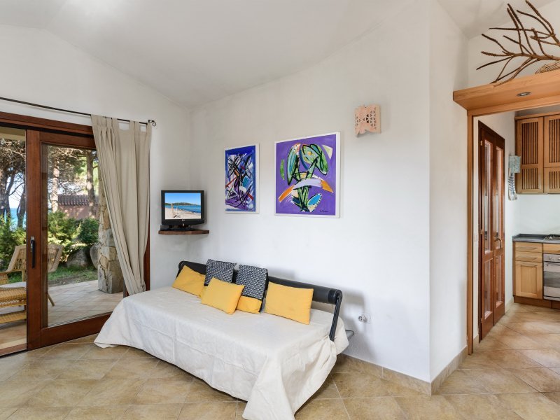 Breites Sofa im Wohnzimmer von Casa Grazia, dahinter ein kleiner TV, die große Terrassentür zum Garten und der Zugang zur Küche Breites Sofa im Wohnzimmer von Casa Grazia, dahinter ein kleiner TV, die große Terrassentür zum Garten und der Zugang zur Küche